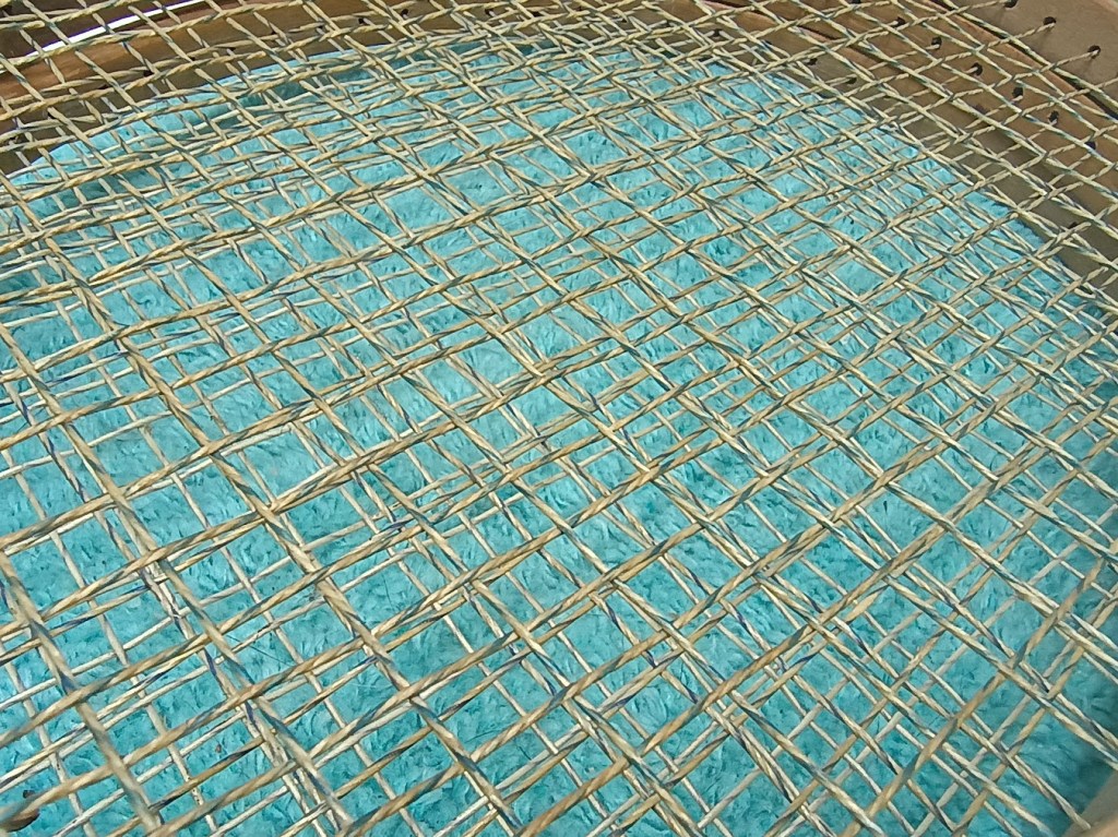 Close-up of a woven pattern made of natural materials layered over a turquoise surface.