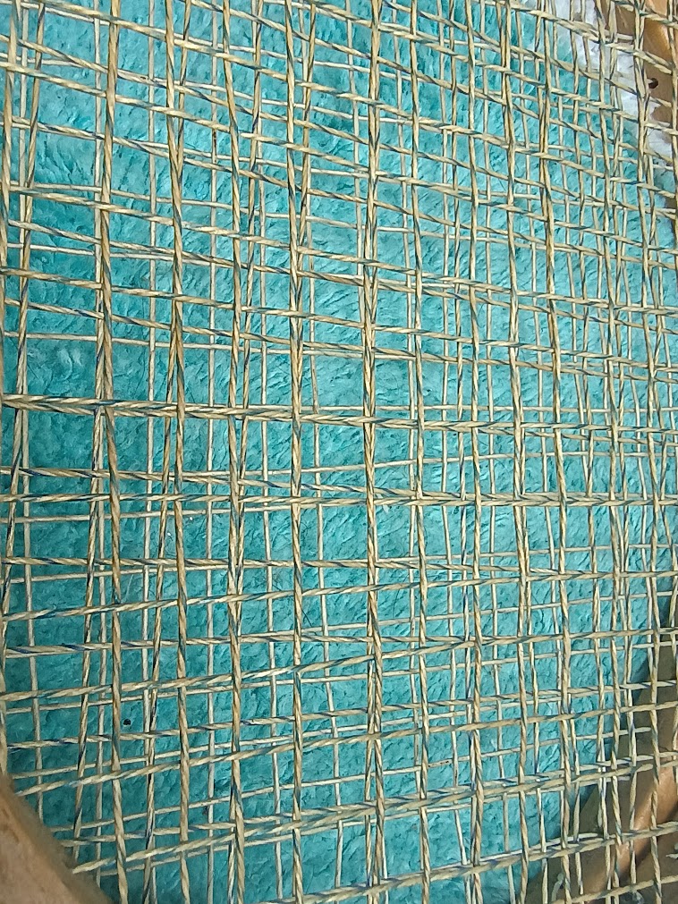 Close-up of a woven textile with a turquoise background and beige threads arranged in a grid pattern.