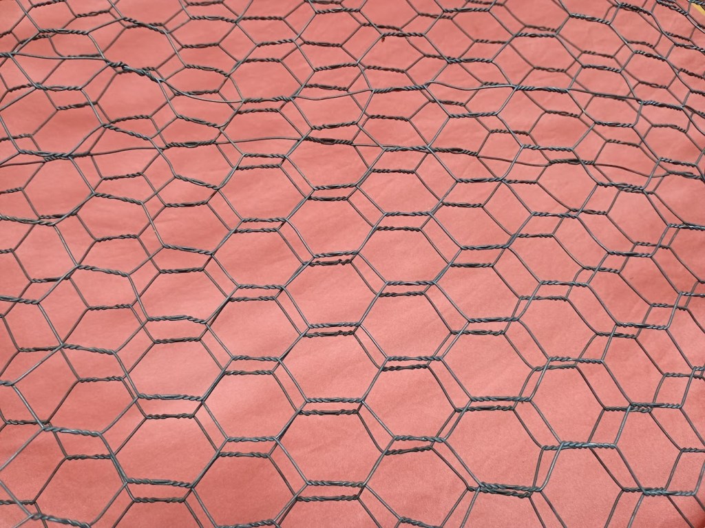 Close-up view of hexagonal chicken wire fencing resting on a pink surface.
