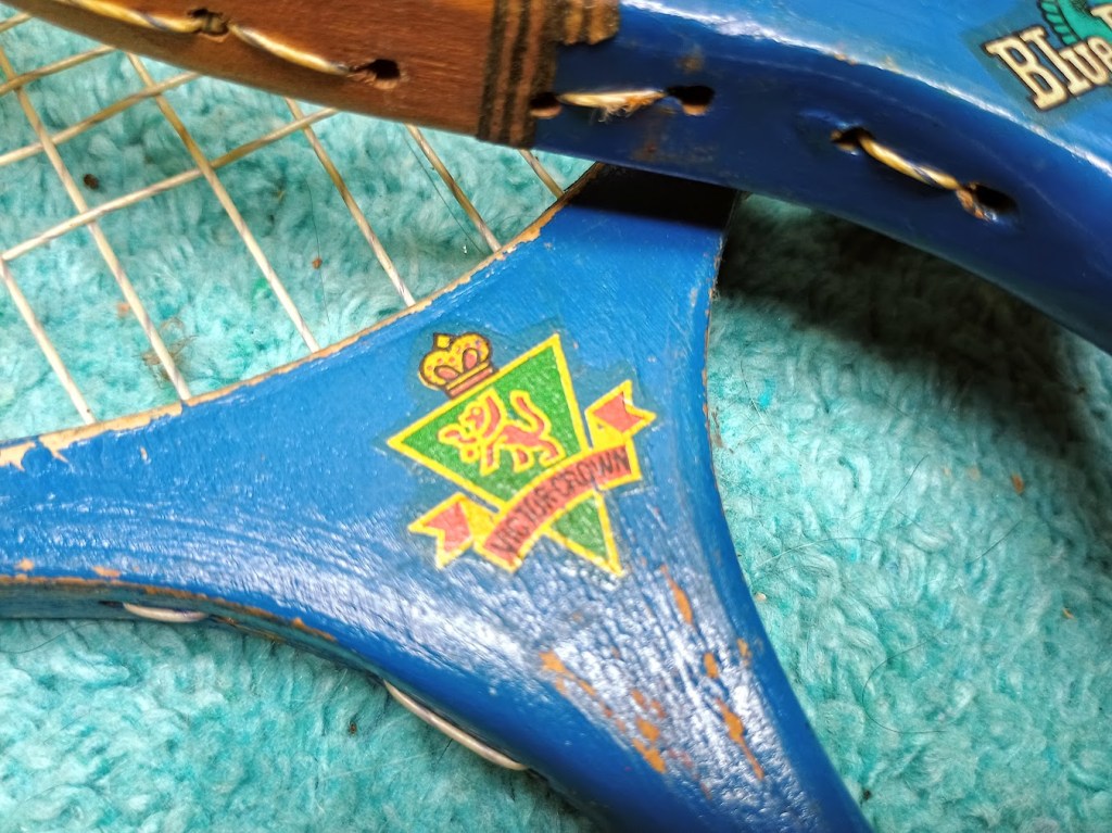 Close-up of a blue tennis racket's handle featuring a colorful logo with a lion and crown design.