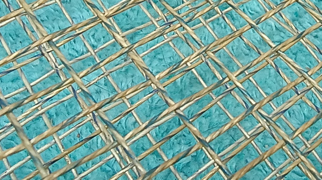 Close-up view of a textured surface featuring an intricate woven design, with natural fibers crossing over a bright turquoise background.